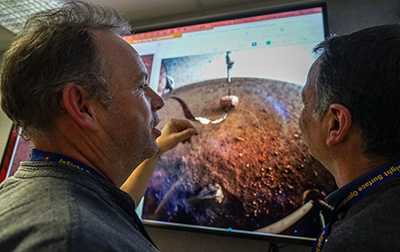 Nicolas Verdier (performance manager at CNES, on the left) and Michel Nonon (command and control manager at CNES, on the right) in front of the first picture taken by the ICC showing the SEIS seismometer on the Martian soil (© NASA/JPL-Caltech/IPGP/Philippe Labrot).